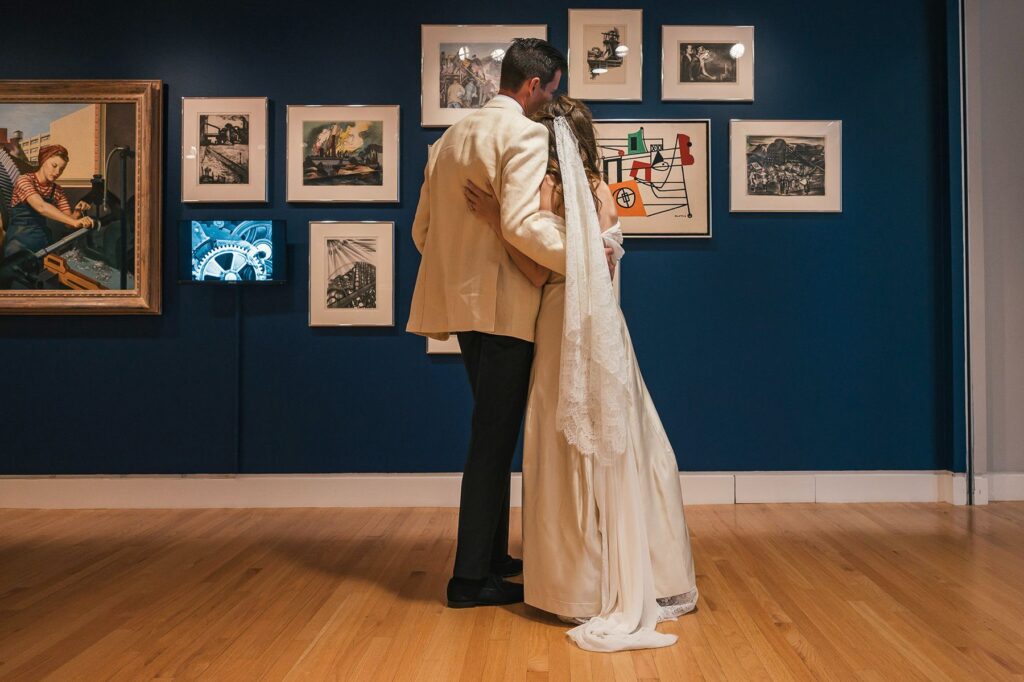 Newlyweds embrace in front of art gallery wall